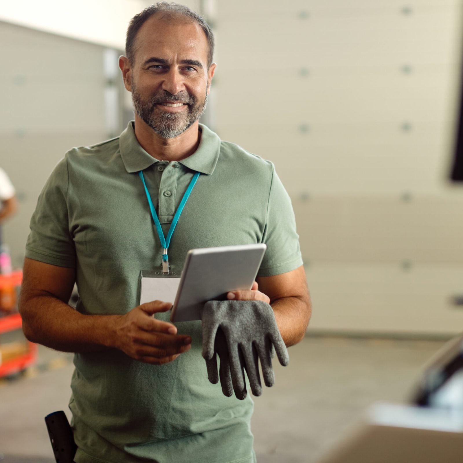 Happy manager working on digital tablet while standing i auto repair shop and looking at camera.